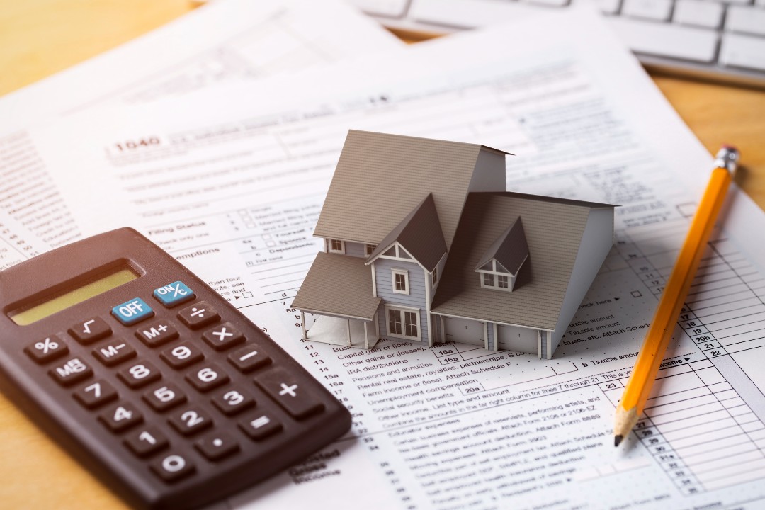 Calculator, house model and pencil lying on piles of documents